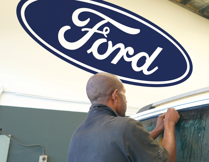 Technician beneath a Ford oval sign in a PNG Motors workshop